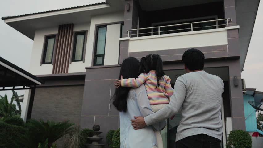 happy family, father and mother holding with child girl while standing in front of their modern house