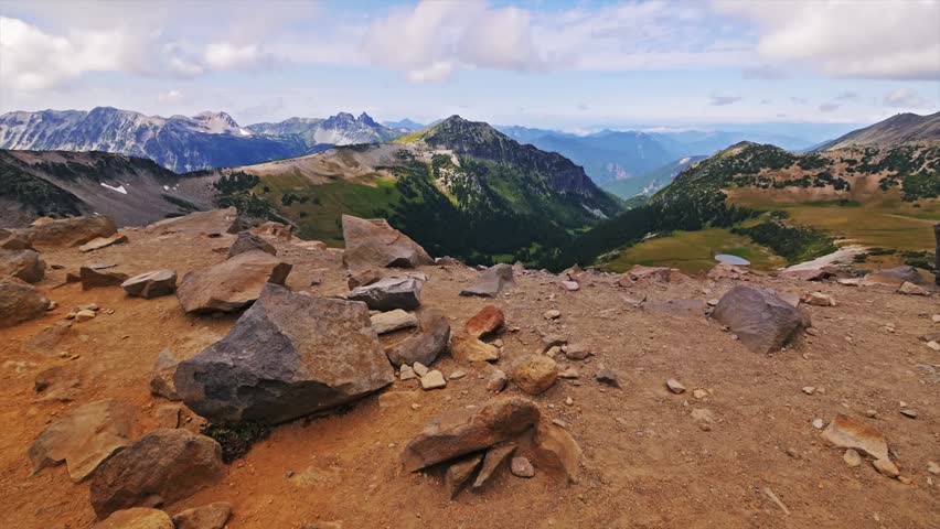 panoramic view from the rocky slopes of the Burroughs Mountain Trail in Mount Rainier National Park, Washington. The image captures the rugged alpine landscape, distant peaks, and a valley with green