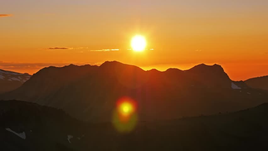 wide-angle view of a golden sunrise over the jagged silhouettes of the Burroughs Mountain Trail in Mount Rainier National Park, featuring a deep orange sky and cinematic lens flare.
