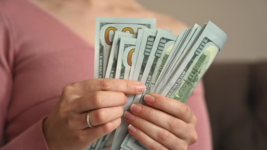 Woman hands counting stack of hundred dollar bills in slow motion close up footage of cash movement.
