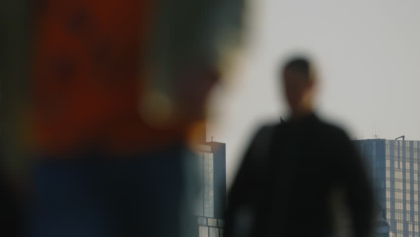 Urban skyline glass skyscrapers under soft morning or evening light, observation deck with people visible on rooftop in distance, blurred pedestrians moving in foreground, calm city lifestyle scene