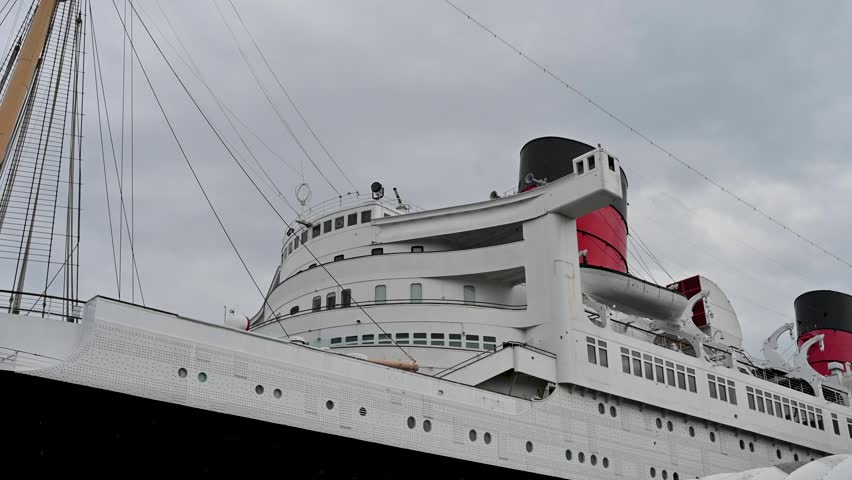 A vintage ocean liner with white superstructure and red funnel moored at a dock.