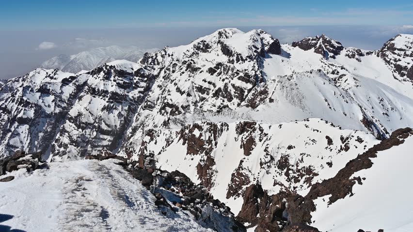 Stunning aerial panorama of snow covered peaks of the Atlas Mountains. The breathtaking mountain range stretches across the horizon under a clear sky