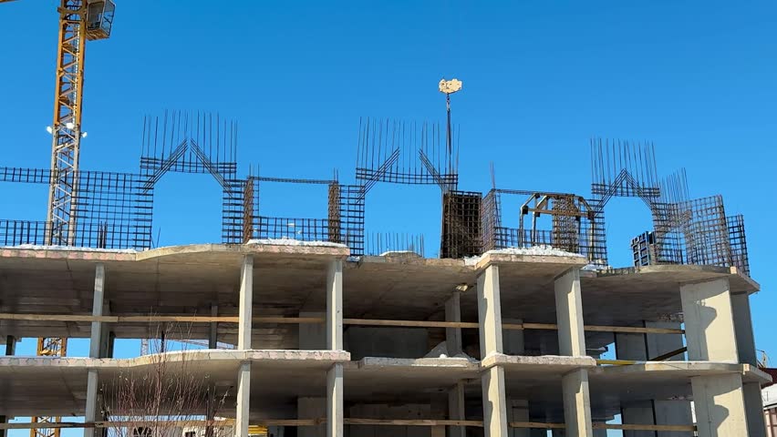 Unfinished concrete apartment building under construction, sunny blue sky, tower crane towering above exposed slabs and columns