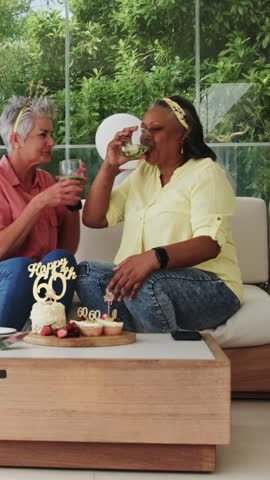 Vertical video: Senior women friends clinking glasses over cake and scrolling smartphone on patio. Celebration, friendship, aging, outdoor, leisure, happiness, vertical video