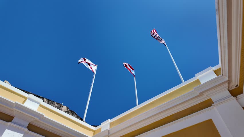 San Juan, Puerto Rico - April 1st, 2026: Looking up from the Main Plaza (Plaza Principal) inside the Castillo San Felipe del Morro historic fort in San Juan, Puerto Rico. There are 3 flags flying: the Burgundy Cross, the flag of the Commonwealth of Puerto Rico and the United States of America flag.