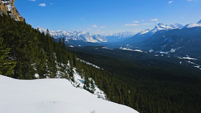 Wide landscape view of a forested valley framed by towering mountains and reflective water, capturing serene wilderness, dramatic elevation, and clear weather in a natural setting.