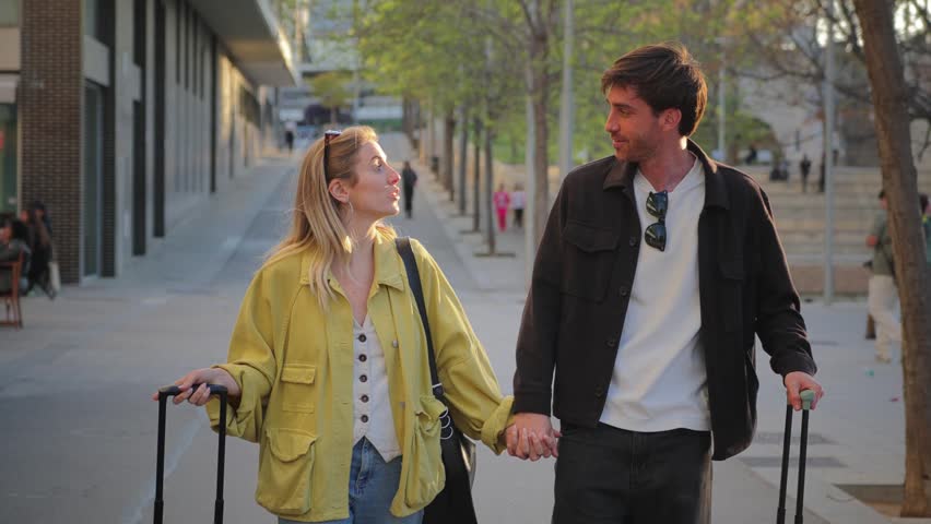 A happy couple is walking together while holding hands and pulling their luggage, excited about their travel plans. Their smiles show the joy of exploration and new experiences ahead.