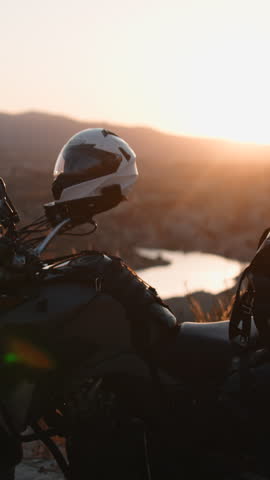 Biker with backpack putting on helmet watching a sunset over the mountains