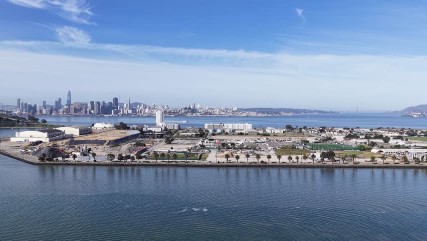 Aerial zoom in view over the water toward treasure island, revealing the stunning San Francisco city skyline, bay bridge, and calm blue bay water under a bright morning sky