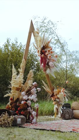 Vertical video. Wooden arch for an outdoor wedding ceremony. Pastel floral arrangements, dried flowers, wooden chairs and an old-fashioned rug. Rustic wedding ceremony