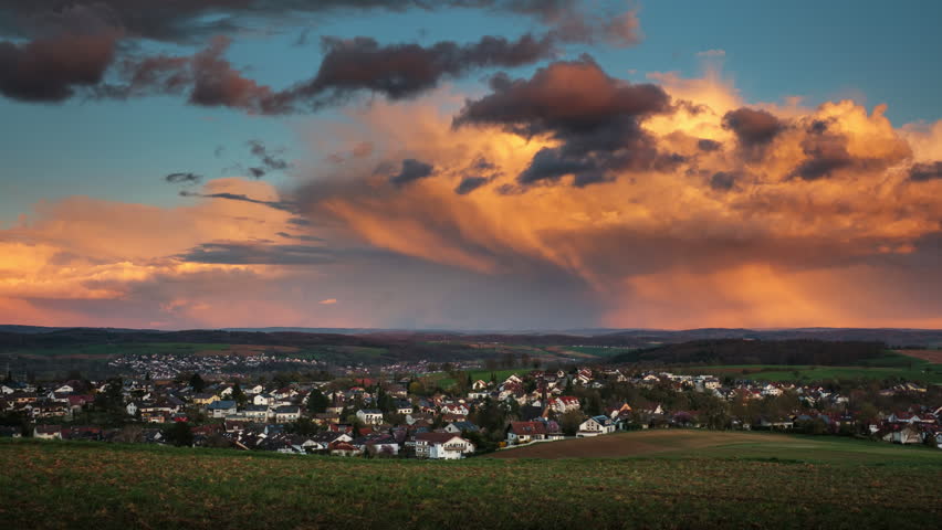 Time lapse of illuminated orange rain clouds over a scenic village. Dramatic sunset sky over rural landscape.