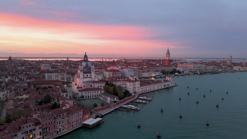 Venice aerial sunset over lagoon, boats gliding past basilica santa maria della salute, pastel sky casting. Italy