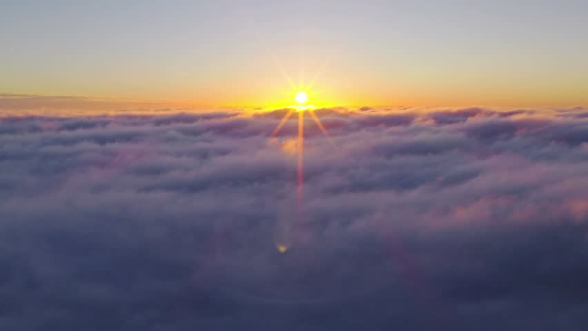 Aerial flight above glowing clouds at sunset with golden sunlight breaking through. Cinematic skyscape with soft fog, warm colors and dramatic atmosphere high above the horizon.