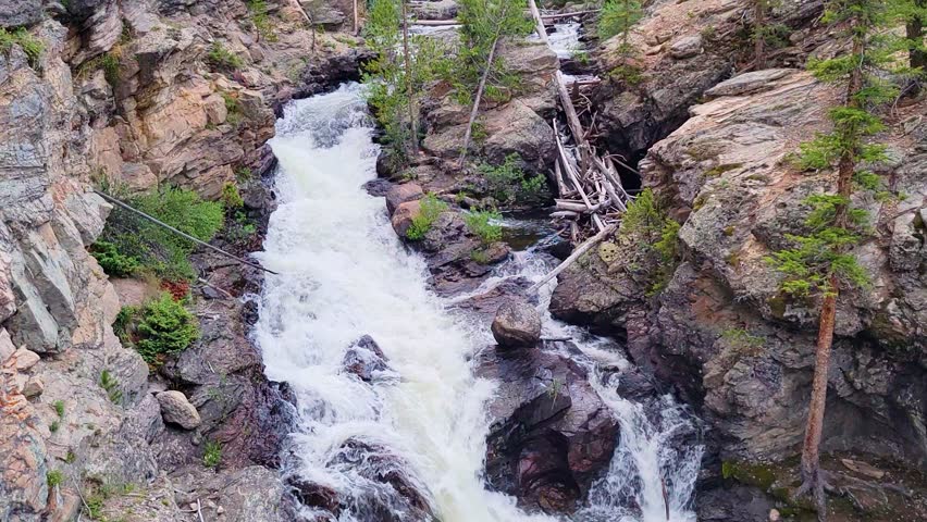Waterfall flowing through a rocky gorge in a landscape resembling Banff National Park, with evergreen trees, rugged canyon walls, and rushing whitewater in a scenic mountain setting.