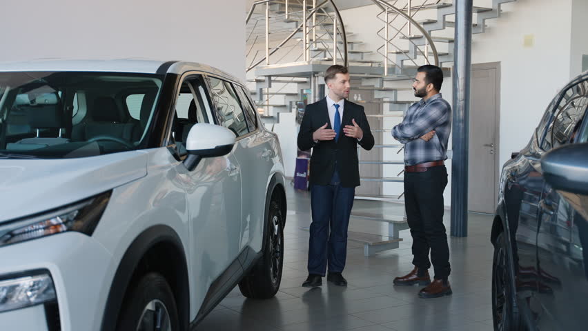 Car salesman showing new suv to Indian customer in dealership showroom