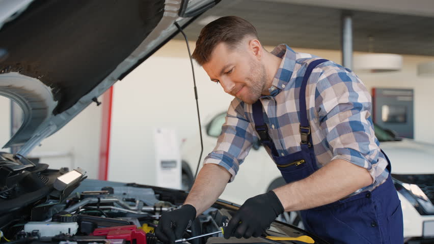 Professional car mechanic repairing engine with screwdriver