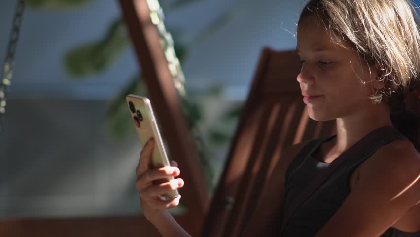 A girl with a smartphone swings on a swing in the waiting room of a train station or airport, the sun