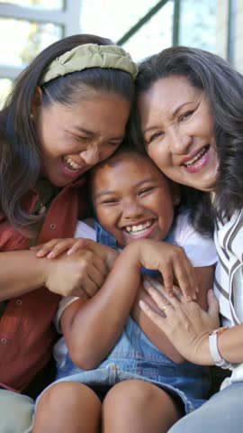 Vertical video: Sharing laughter, family leaning on porch, camera panning right, child in overalls. Multigenerational, kinship, laugh, smile, togetherness, denim, vertical video