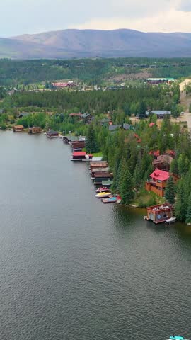 Vertical aerial panorama of a lakeside alpine town with roads, waterfront lodging, evergreen trees, and mountain ridges surrounding a serene high elevation landscape
