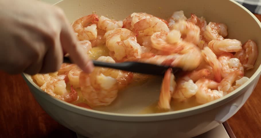 Close up of shrimp being cooked in a frying pan with a spatula. seafood preparation process in the kitchen, fresh shrimp frying, home cooking scene, preparing a healthy meal