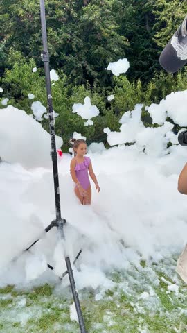 A child enjoys playing in a large pile of foam at an outdoor party. Friends and family gather in the backyard, creating fun and laughter under the sun.