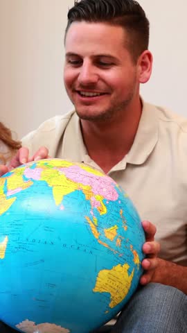 Happy young family sitting on sofa looking at globe at home in the living room