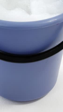 Cleaning sponge falling in to bucket of soap suds against white background