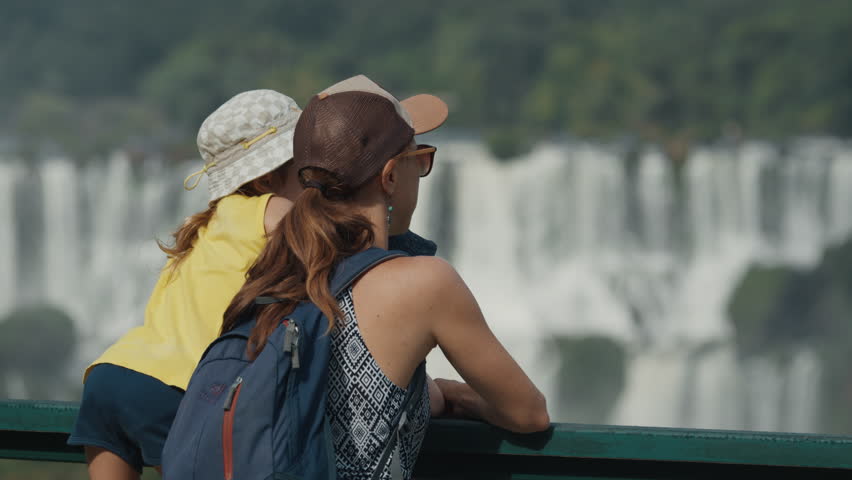 Woman with kids watch powerful Iguazu waterfall with strong flow of the water from a distance