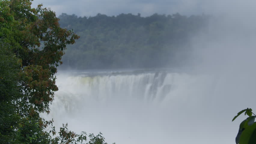 Powerful Iguazu waterfall with strong water flow surrounded by green trees