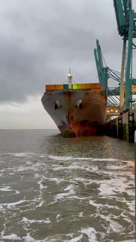 Large bow of a cargo ship with containers in the port and loading cranes