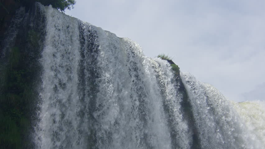 Powerful Iguazu waterfall with massive water flow, mist and foam under cloudy sky