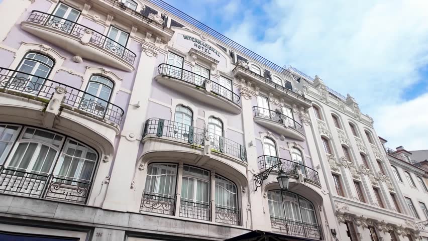 Upward street view of ornate Internacional Hotel, a historic building with balconies and classic architecture in downtown Lisbon, Portugal under a blue sky.