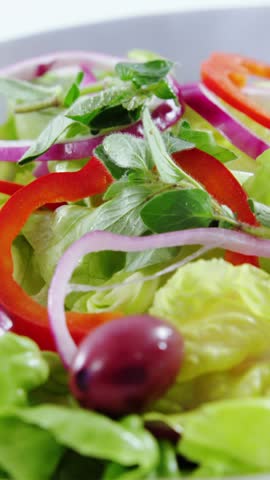 Vertical video: Salad plate on white backdrop, camera moving up revealing olive drop, showing color. Closeup, greens, onion, pepper, herb, vegetables, vertical video