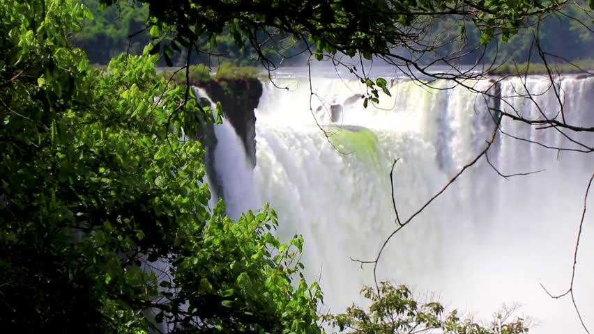 Foz do Iguacu Iguazu Falls waterfall fall waterfalls cascade cascades in tropical nature rainforest behind trees panorama view blue sky and turquoise green water Parana Brazil and Misiones Argentina.