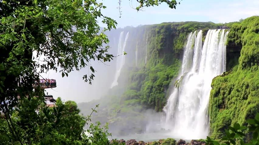Foz do Iguacu Iguazu Falls waterfall fall waterfalls cascade cascades in tropical nature rainforest behind trees panorama view blue sky and turquoise green water Parana Brazil and Misiones Argentina.