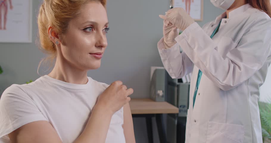 Immunization of adult woman in hospital for flu and coronavirus prevention, doctor in gloves giving shot of vaccine to patients arm. Girl sitting, waiting for vaccination with trust, nurse injecting