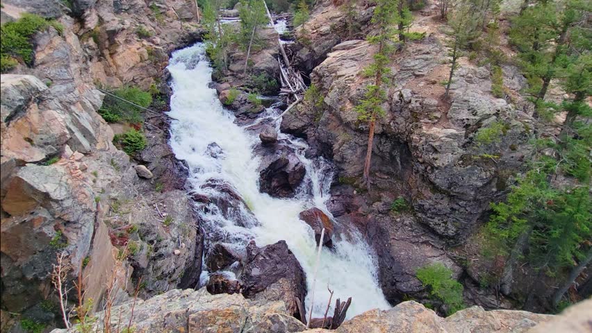 Scenic forest waterfall in a setting reminiscent of Banff, with whitewater carving through weathered rock formations and evergreen woodland in a rugged mountain wilderness environment.