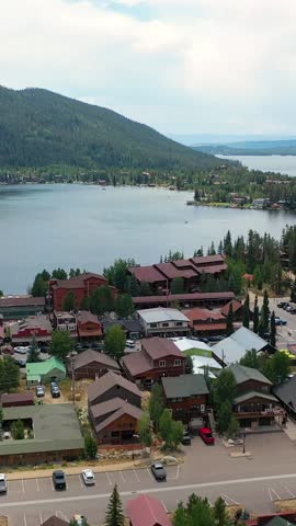 Portrait drone panorama across Grand Lake Colorado showing the lakeside town edge, marina docks, calm mountain water, and evergreen slopes rising toward distant peaks