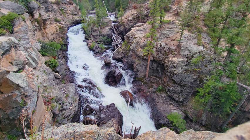 Mountain stream and rocky waterfall in a setting similar to Rocky Mountain National Park, featuring evergreen forest, steep canyon walls, and scenic Colorado wilderness terrain.