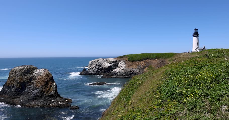 Yaquina Head Lighthouse standing on a grassy cliff with ocean waves crashing against the rocky shore.