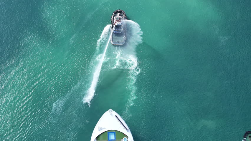 luxury cruise ship escorted by three tugboats in clear turquoise ocean water. One tugboat performing a ceremonial water salute. Travel, tourism, and maritime leisure.	