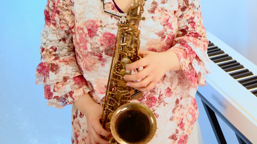 A woman playing the saxophone in front of a keyboard