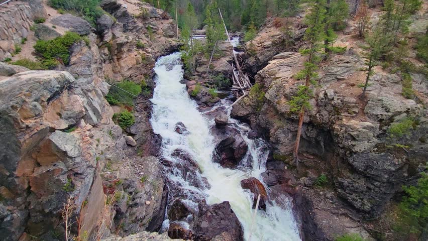 Forest waterfall view evocative of Rocky Mountain National Park, with cascading rapids, granite rock formations, and pine trees creating a dramatic high country Colorado landscape.