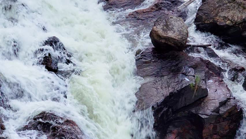 Powerful mountain waterfall cascades through a narrow rocky gorge surrounded by conifer trees, showcasing textured cliffs, flowing rapids, and scenic alpine style wilderness scenery.