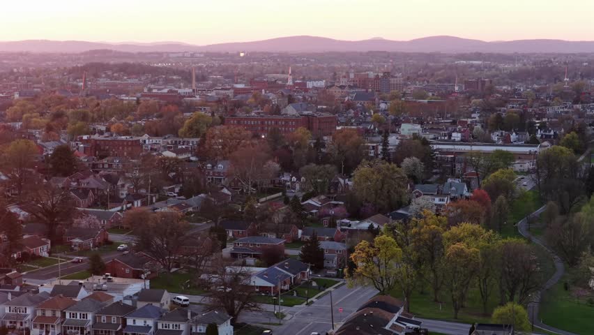 Aerial view of York town, Pennsylvania with residential suburb, red brick houses, tree lined streets and downtown skyline in background under warm spring sunset light. Charming town. Wide shot.
