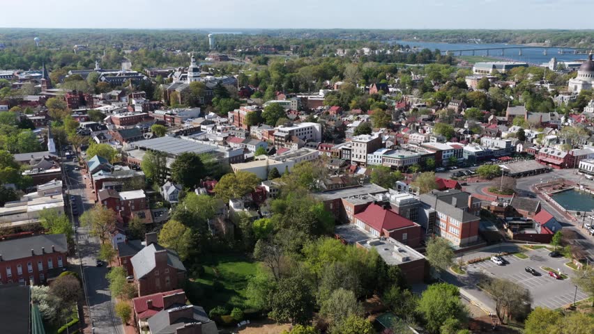 Aerial flyover of Annapolis Maryland historic town with colorful buildings, tree lined streets and waterfront views under bright spring sunlight. Calm atmosphere in charming coastal city. Wide shot.