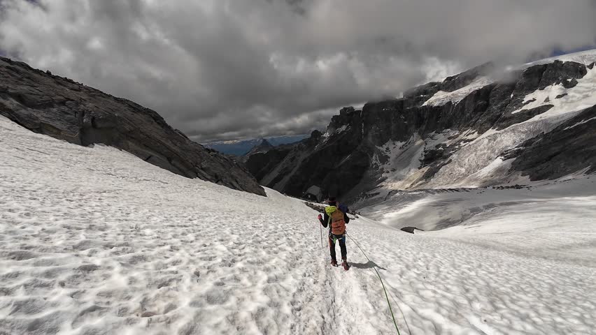 POV mountaineering in rope team with mountaineer descending towards alpine hut Rifugio Guide della Valle d