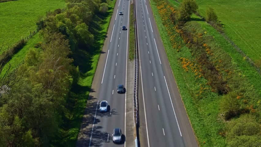 Four-lane highway cutting through green rural landscape in France. Aerial backward