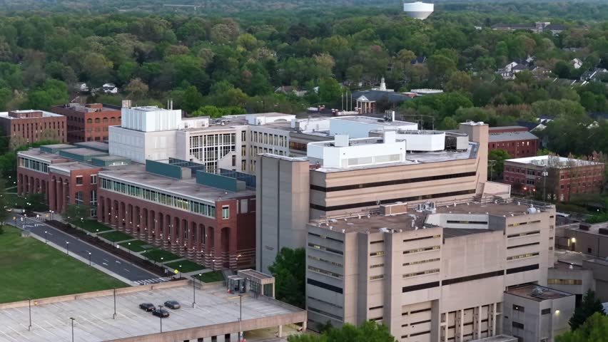 Aerial view of Fairfax County courthouse complex in Fairfax, Virginia, USA during spring with civic buildings, parking garage, government offices, trees and suburban cityscape at dusk light. Wide shot